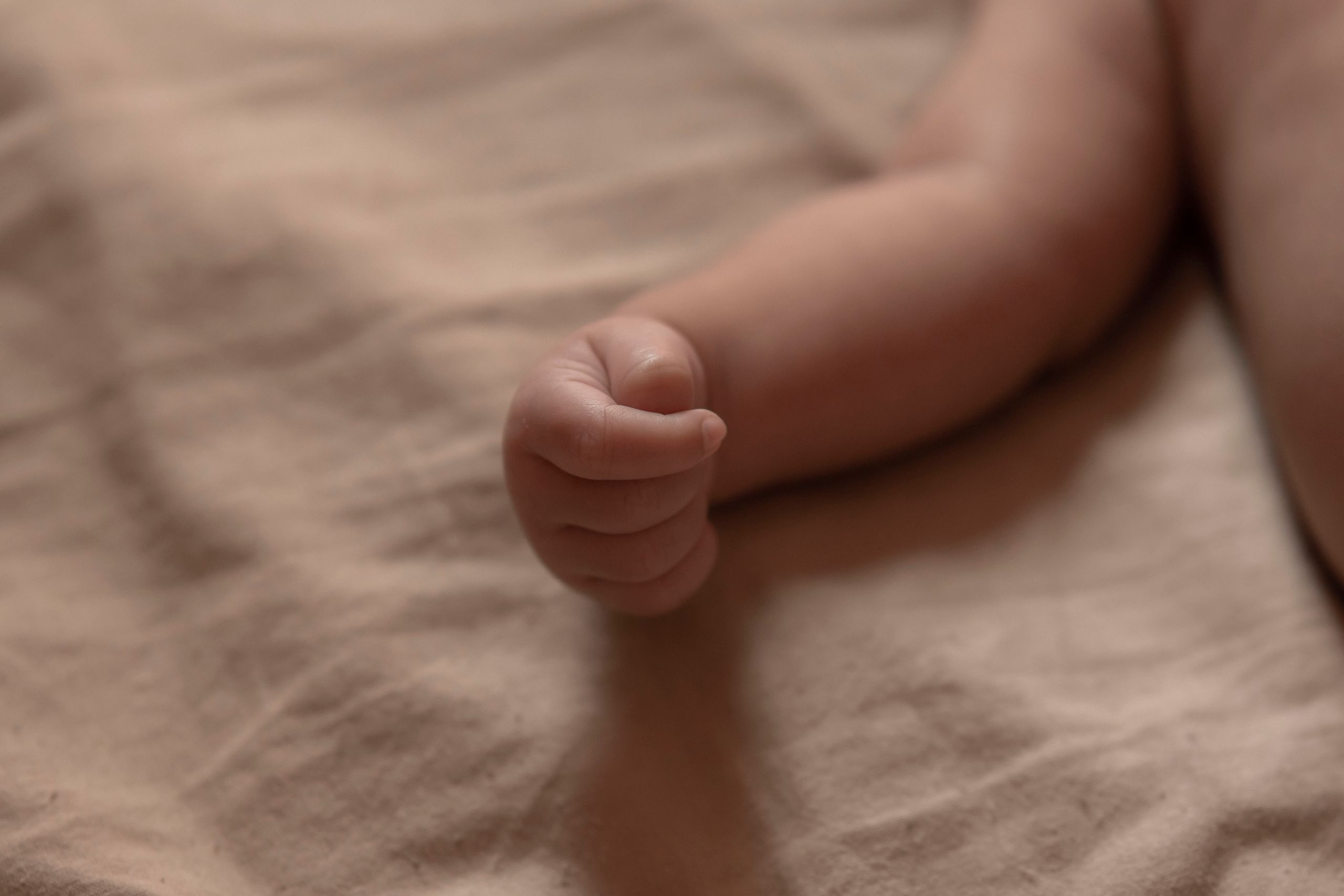 A delicate newborn's hand curled up on a soft beige blanket, capturing innocence.