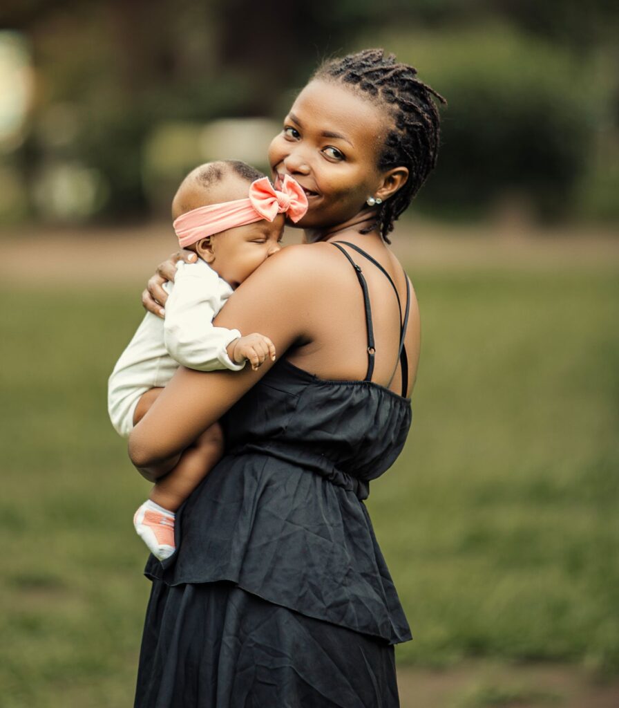 A mother happily holds her baby in a peaceful outdoor park setting.