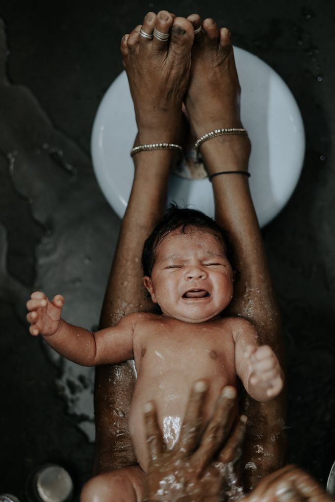 A newborn baby experiencing a traditional bathing ceremony indoors with delicate care.