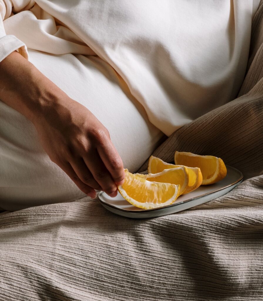 A person picking an orange slice from a plate, resting on light fabric.