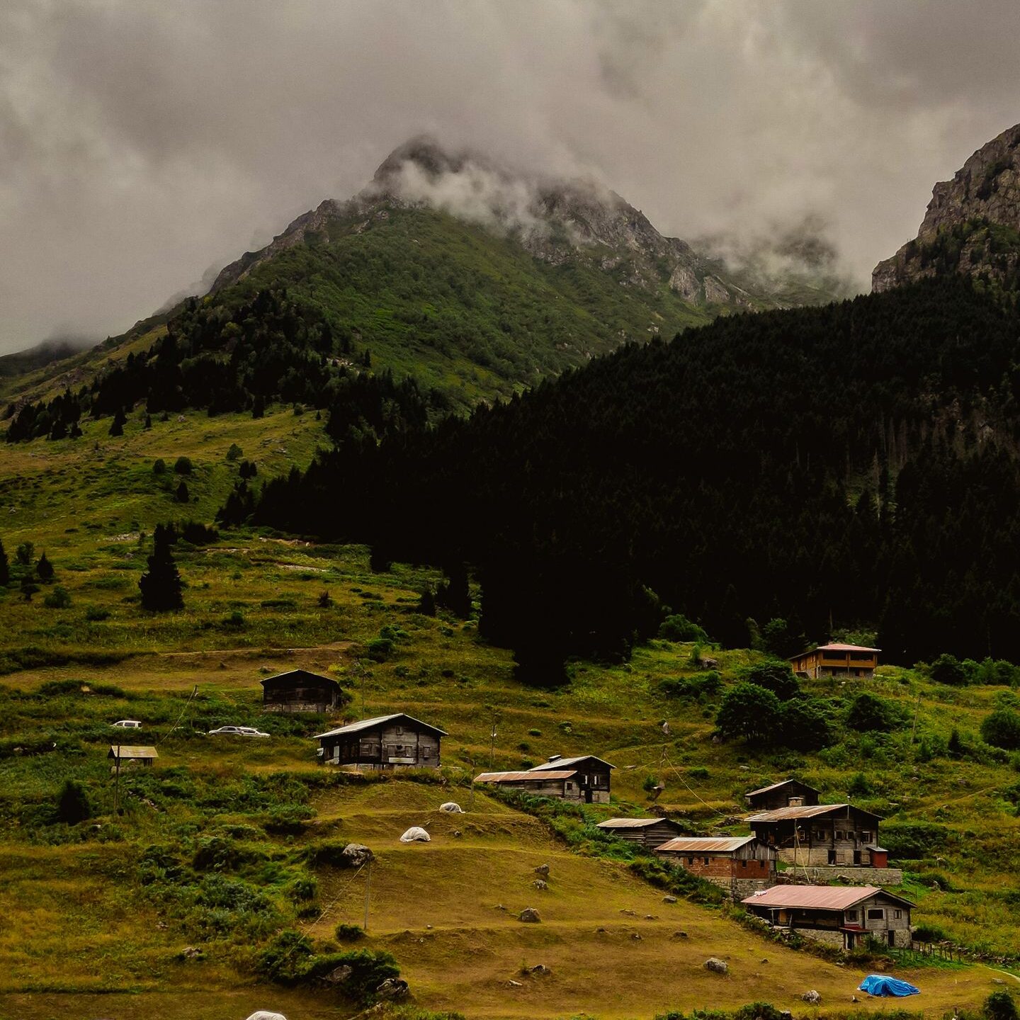 A stunning aerial view of a tranquil mountain village surrounded by lush greenery under a cloudy sky.
