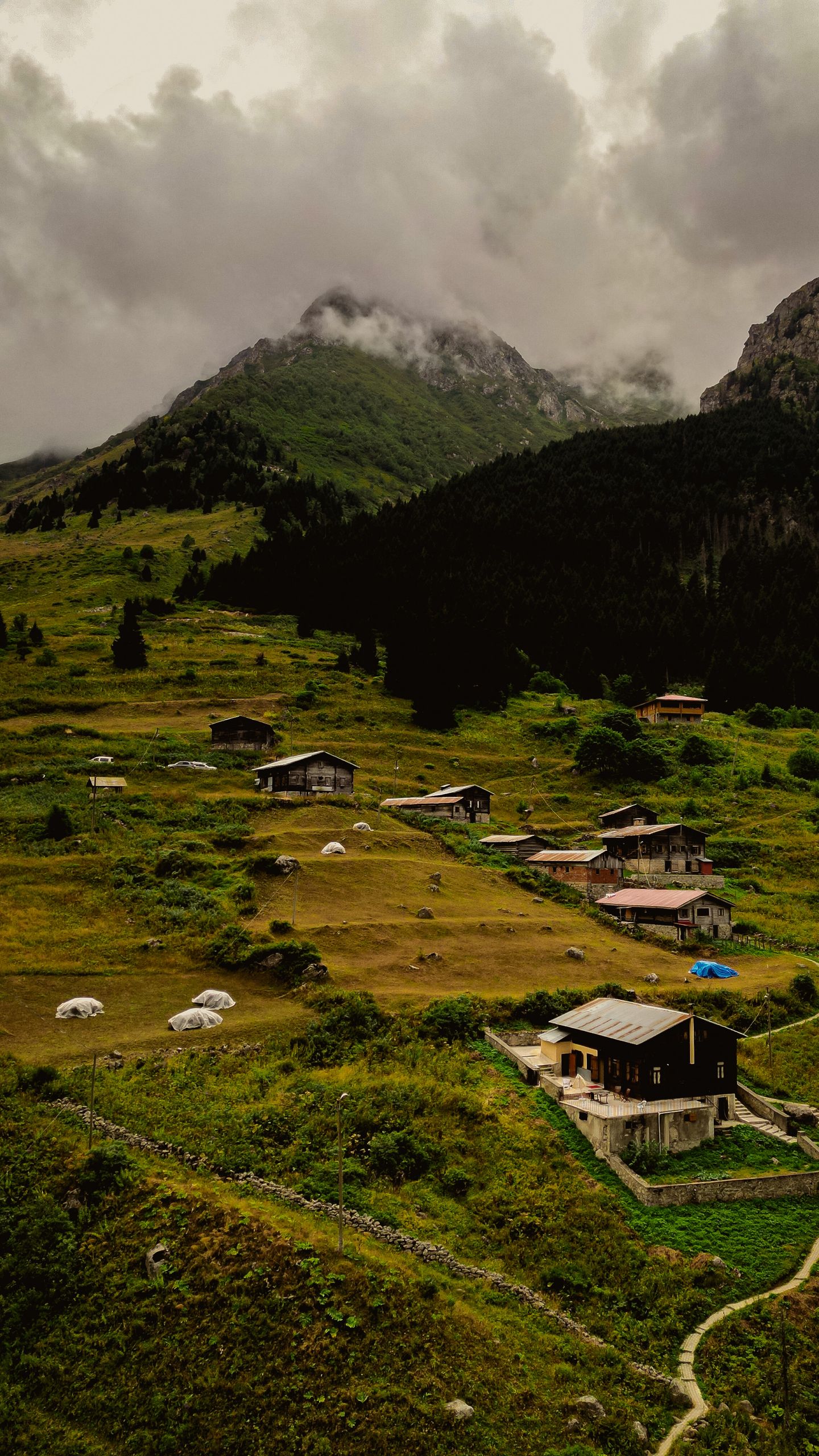 A stunning aerial view of a tranquil mountain village surrounded by lush greenery under a cloudy sky.