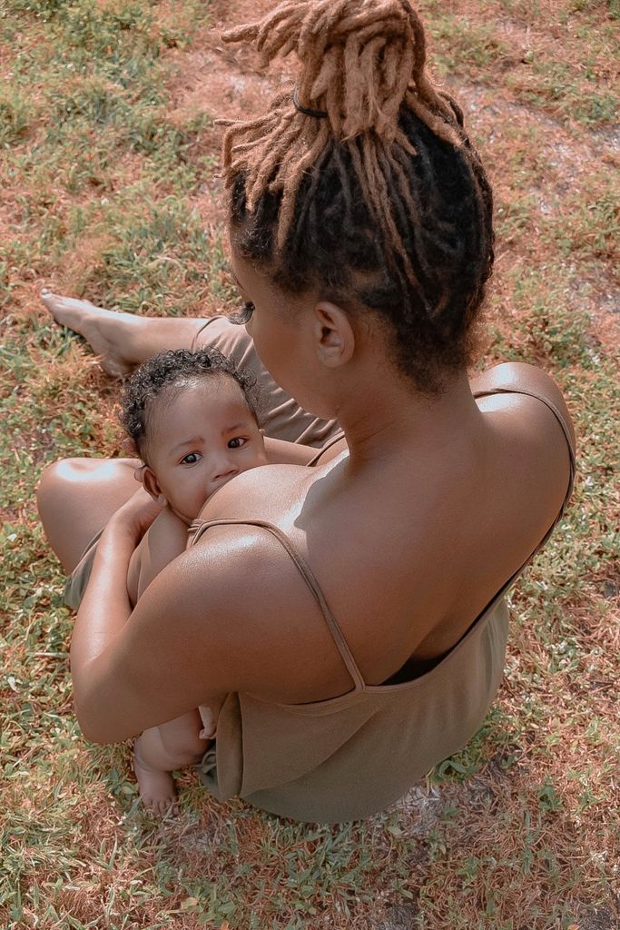 A tender moment of a mother breastfeeding her baby while sitting outside on a sunny day.