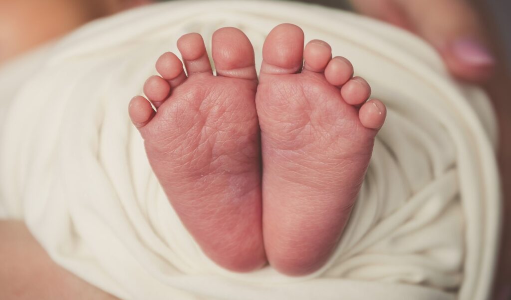 Adorable newborn baby feet wrapped in soft white blanket, capturing innocence and delicacy.