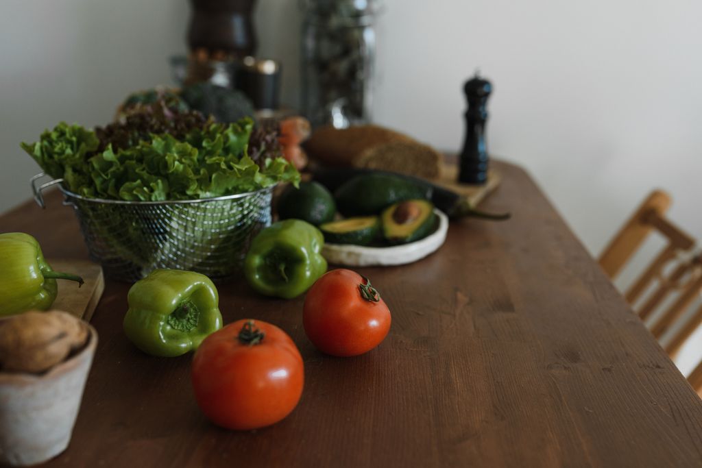 An assortment of fresh vegetables including tomatoes and avocados on a wooden kitchen table.