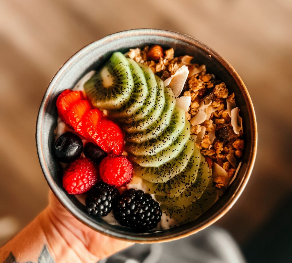 Close-up of a colorful fruit and granola bowl held by a tattooed hand.