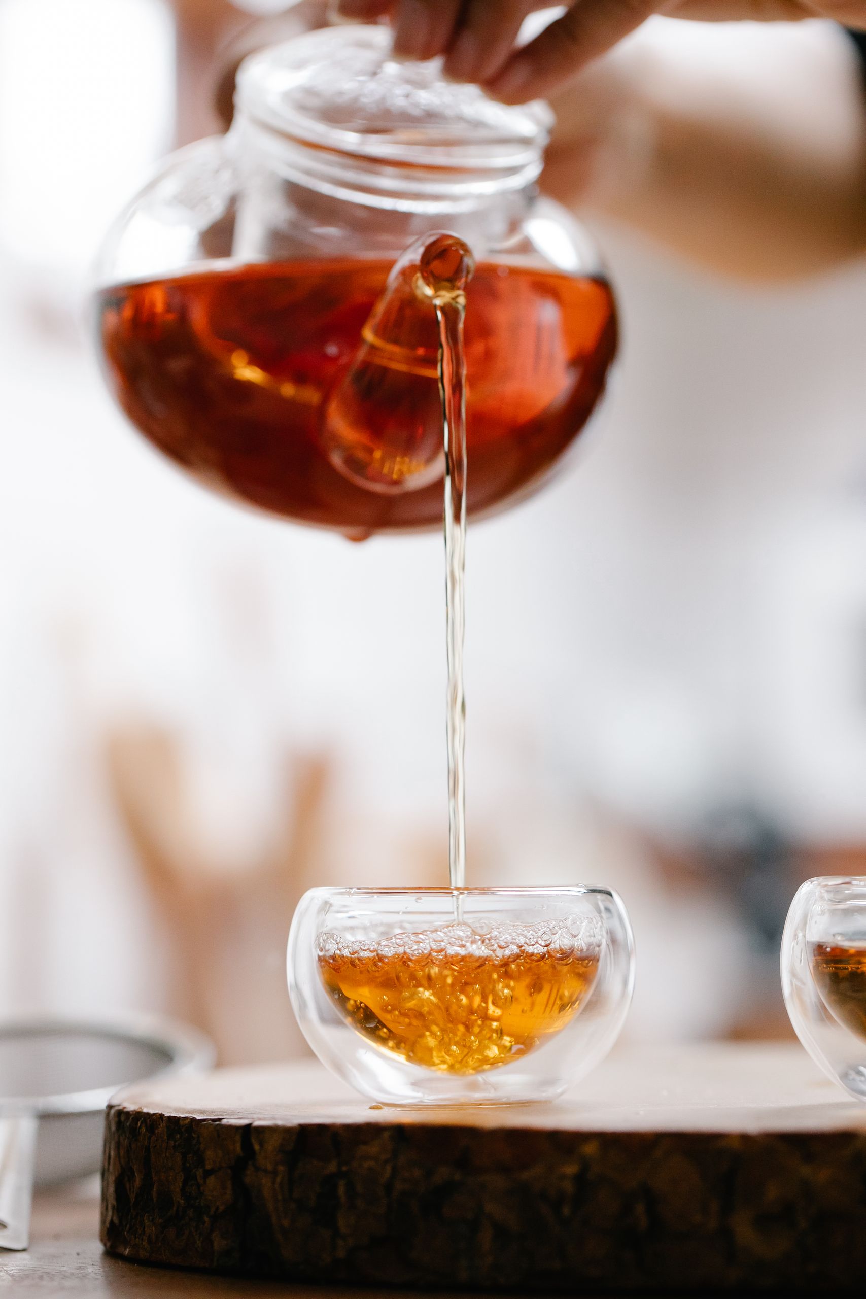 Close-up of herbal tea being poured from glass teapot into teacup. Warm, cozy atmosphere.