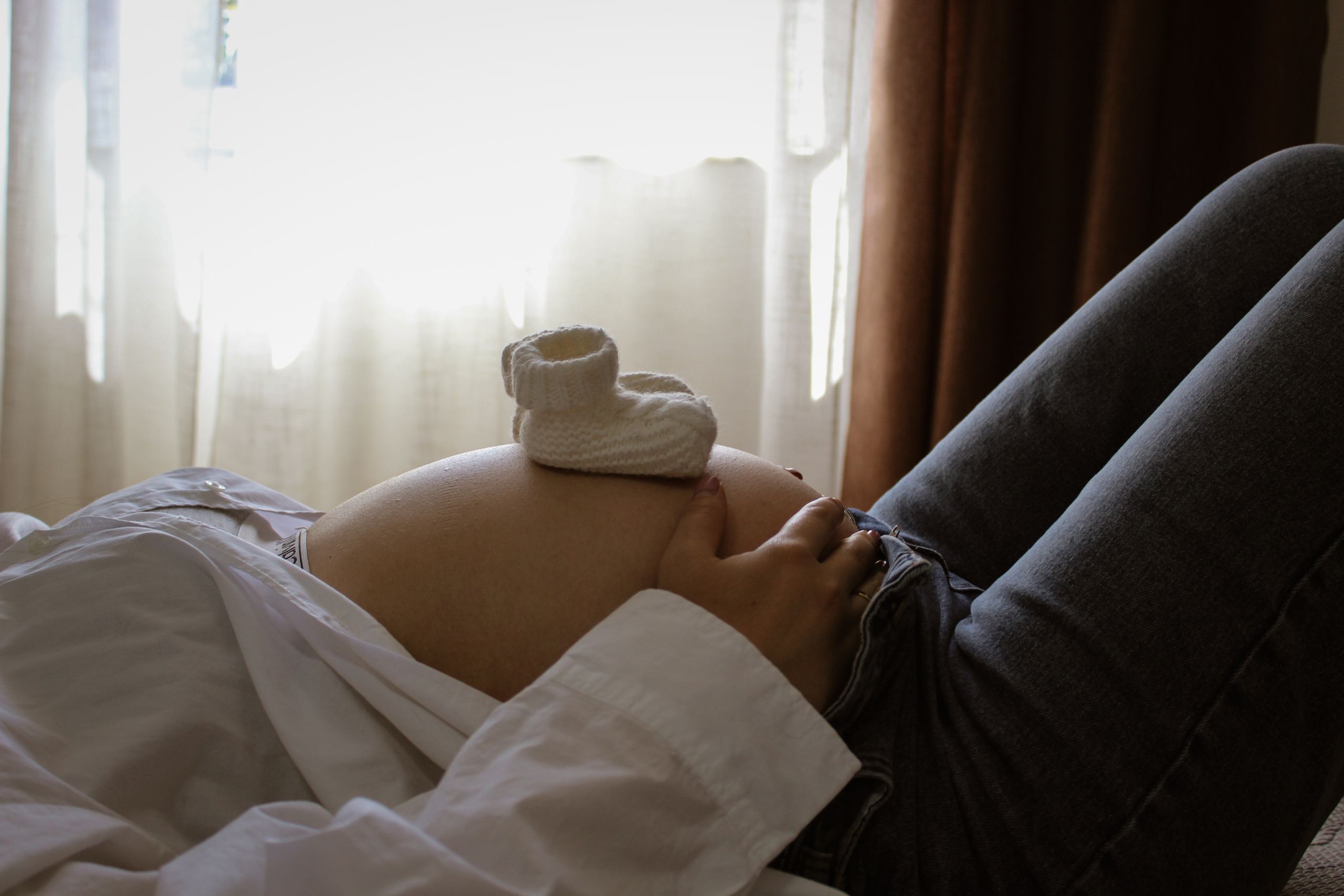 Expectant mother resting with baby booties on her belly, symbolizing anticipation and parenthood.