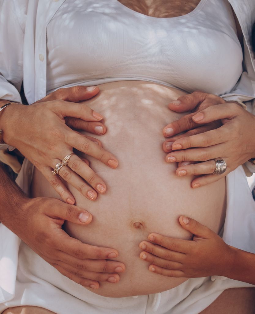 Hands of family members lovingly touching a pregnant belly outdoors, symbolizing unity and new beginnings.